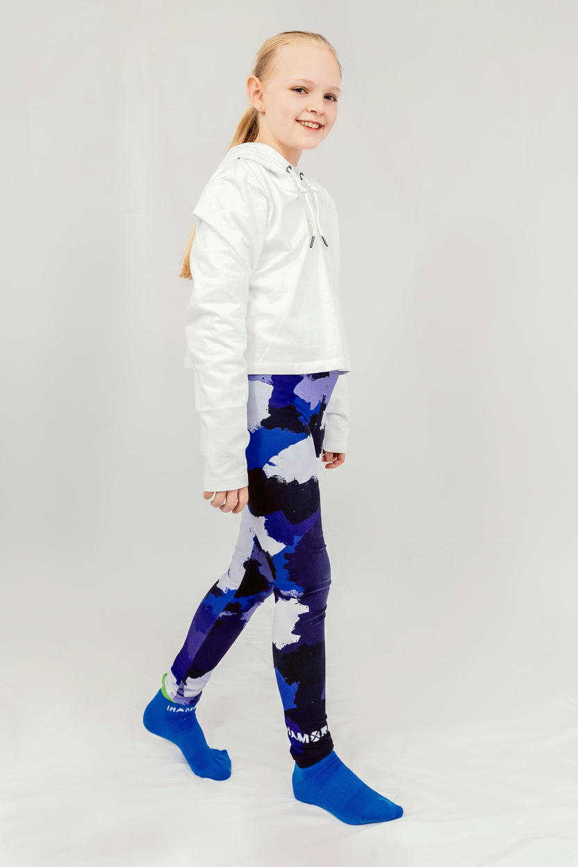 A girl wearing a white hoodie and blue camo leggings, standing against a white background, Girl wearing IHAMORA Blue Camo seamless leggings with bright blue camo pattern.