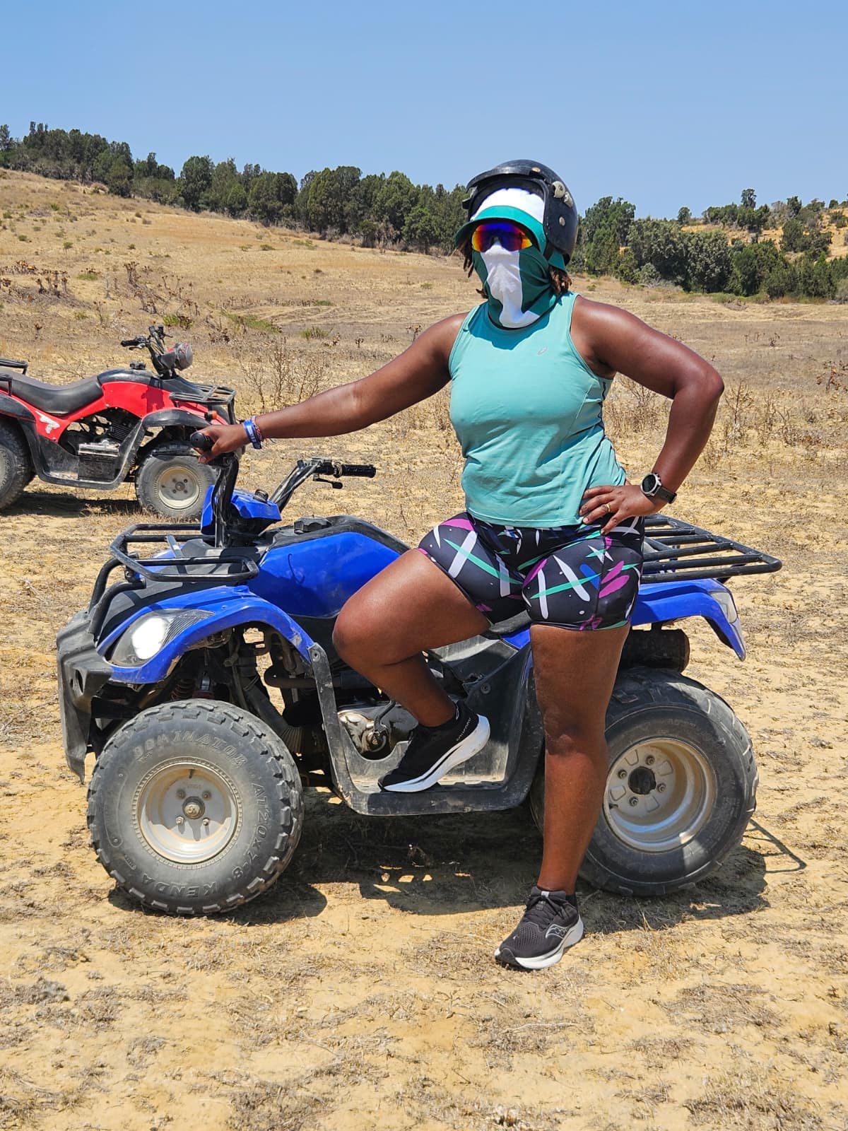 Woman on a blue ATV in an open field with another ATV in the background, wearing high-waisted bamboo gym shorts by IHAMORA