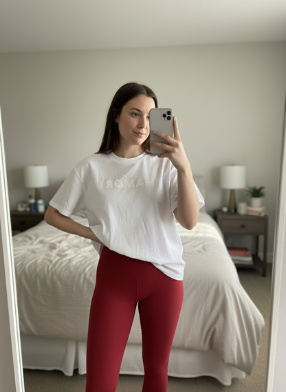 woman taking a mirror selfie wearing a white t-shirt and red leggings in a bedroom.