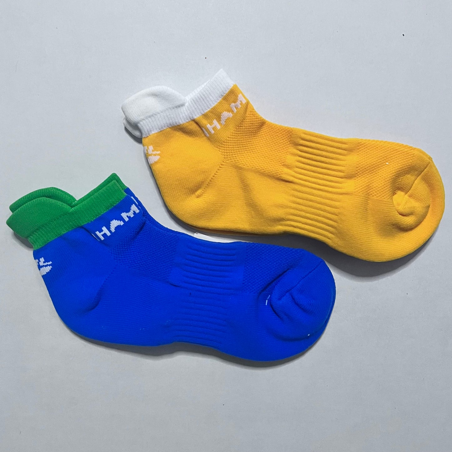 Two socks, one yellow and one blue with green cuff, on a gray background.