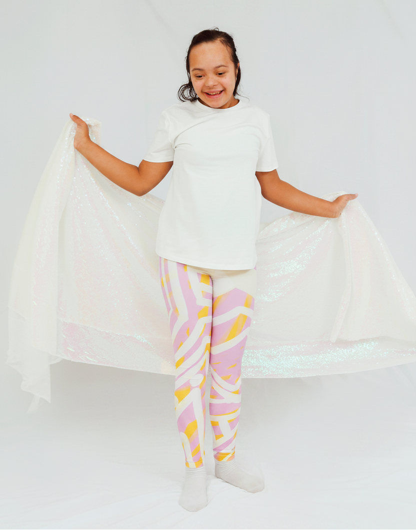 girl wearing a white shirt and colorful pants holding a white fabric against a white background